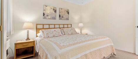 A bedroom with a bed, two bedside lamps, a ceiling fan, and two wall-mounted artworks.