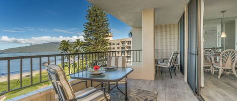 A balcony with a table and chairs, overlooking a beach and ocean.