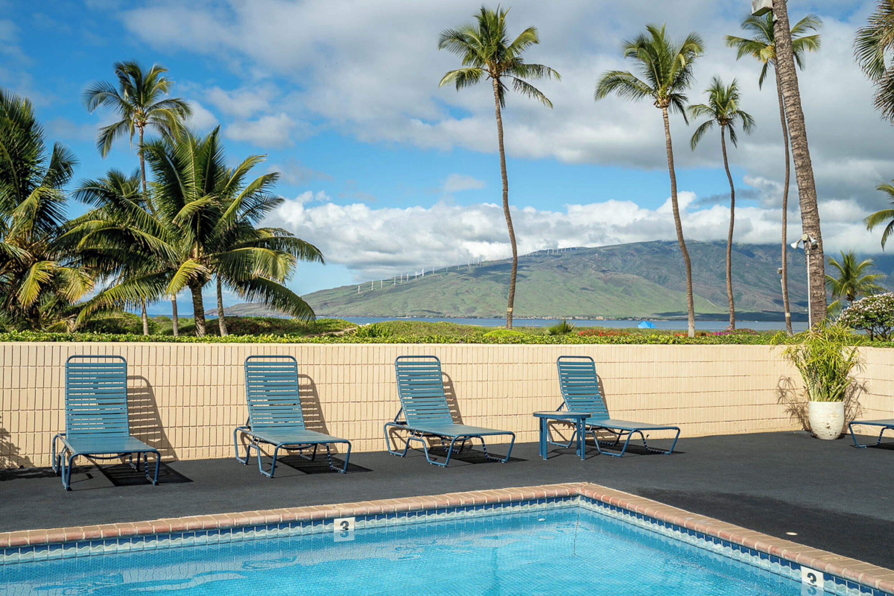 A poolside area with lounge chairs and a view of palm trees and a mountain.