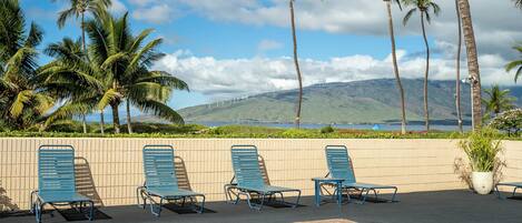 A poolside area with lounge chairs and a view of palm trees and a mountain.
