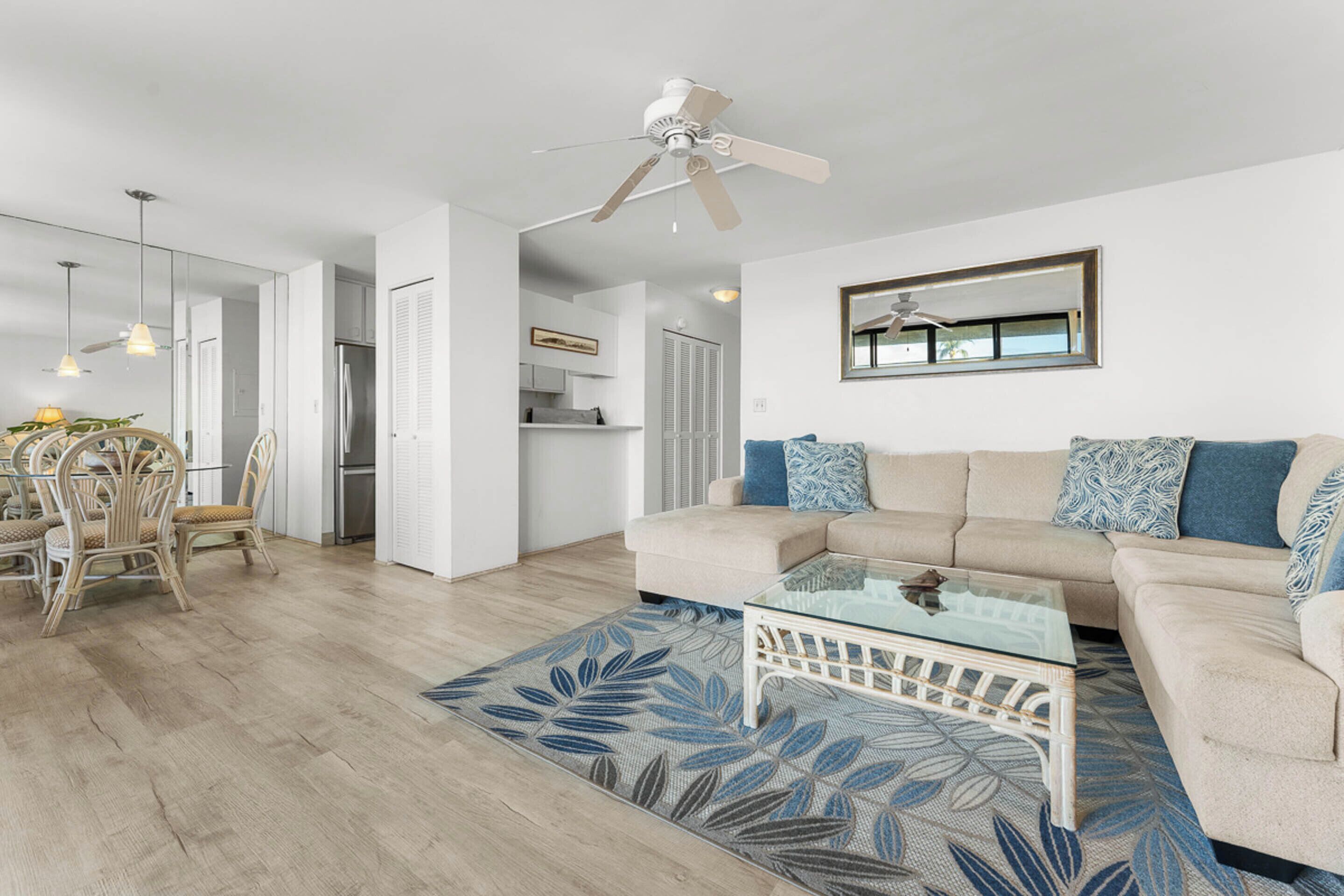 A modern living room with a beige sofa, a glass coffee table, and a dining area with wicker chairs.