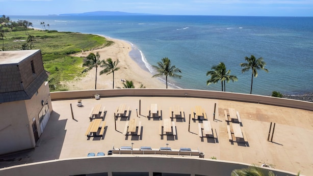 Une vue sur la plage depuis un balcon, avec des chaises longues en bois et un bâtiment doté d’un toit plat.