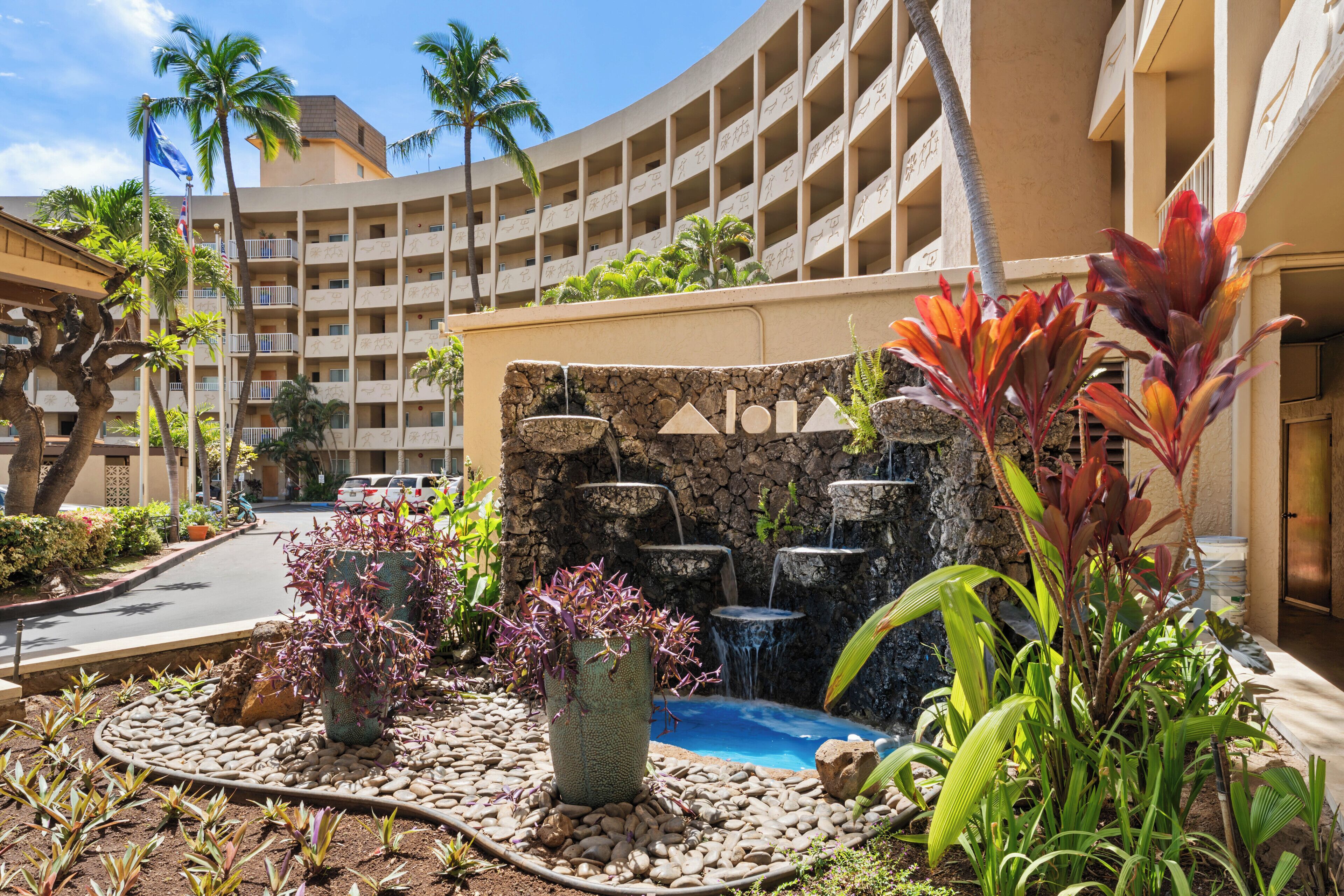 A hotel courtyard with a pool, palm trees, and a waterfall feature.