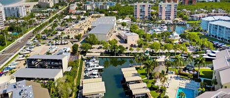 An aerial view of a marina with boats docked, surrounded by buildings and a beach in the background.