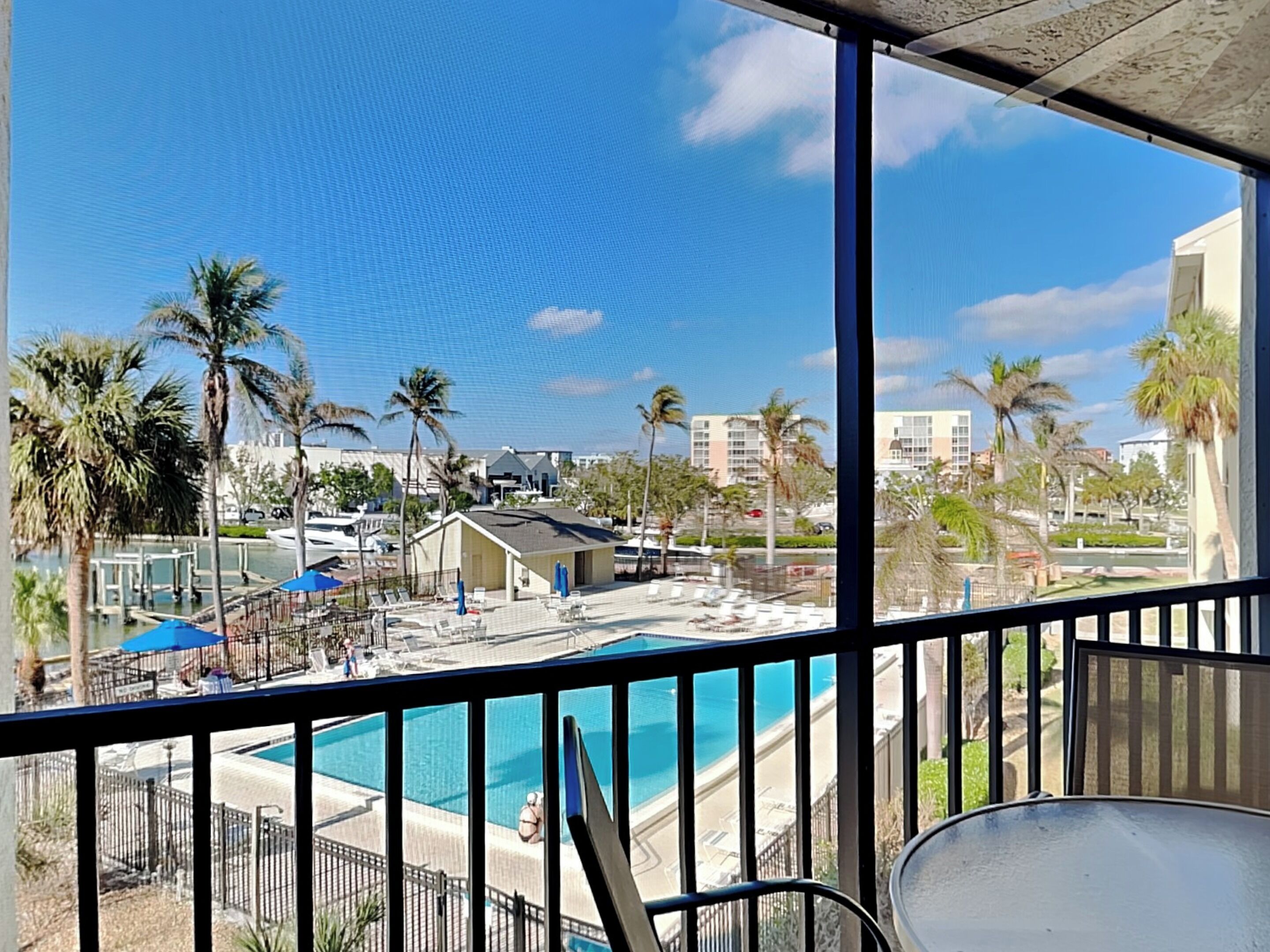 A pool area with lounge chairs and umbrellas, a view of the beach, and palm trees.