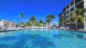 A clear blue pool with lounge chairs and palm trees, surrounded by buildings. - Santa Maria 208 by Distinctive Beach Rentals (Fort Myers Beach)