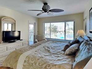 Ein Schlafzimmer mit Bett, Fernseher, Deckenventilator und einem Fenster mit Jalousien.
