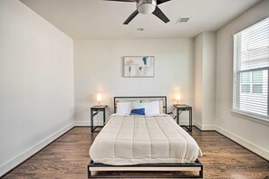 A bedroom with a bed centered on a wooden floor, flanked by nightstands with lamps, a ceiling fan, and a window with blinds. - 3-Story Home Near Museums, Nightlife & Downtown! (Houston)
