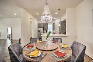 A dining area with a round table set for six, surrounded by grey upholstered chairs. A chandelier hangs from the ceiling, and a vase with flowers is placed on the table. - 3-Story Home Near Museums, Nightlife & Downtown! (Houston)