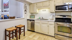 Una cocina moderna con armarios blancos, electrodomésticos de acero inoxidable, lavavajillas y una zona de estar con dos taburetes.