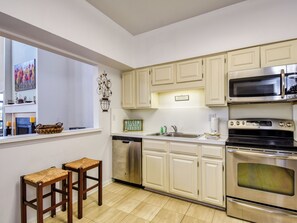 Una cucina moderna con mobili bianchi, elettrodomestici in acciaio inossidabile, lavastoviglie e un angolo relax con due sgabelli.