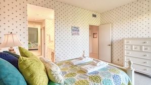 Un dormitorio con cama, cómoda, espejo y una puerta que da a otra habitación.