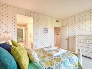 Una camera da letto con un letto, una cassettiera, uno specchio e una porta che dà su un'altra stanza.