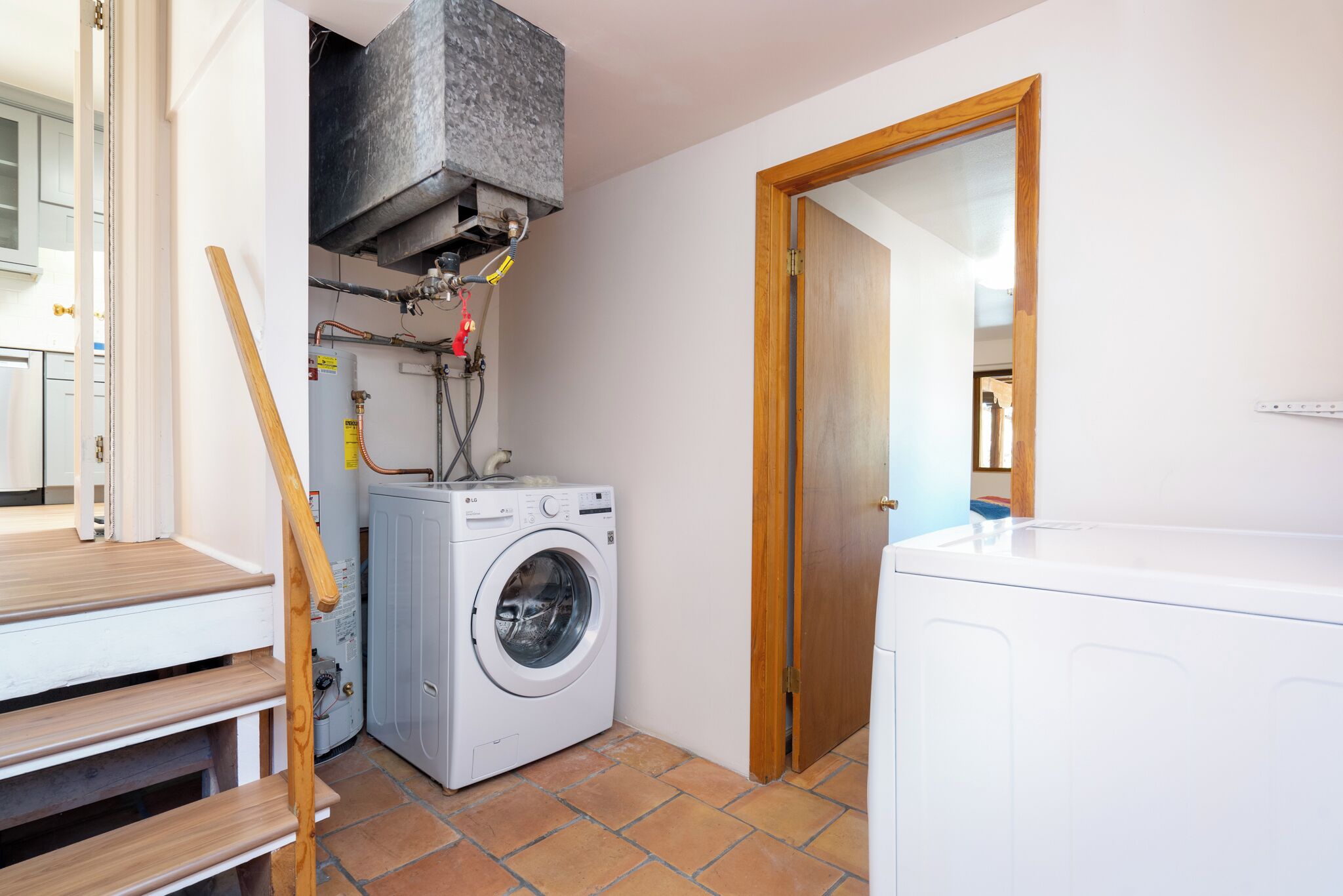 A laundry room with a washing machine, dryer, and a wooden staircase.