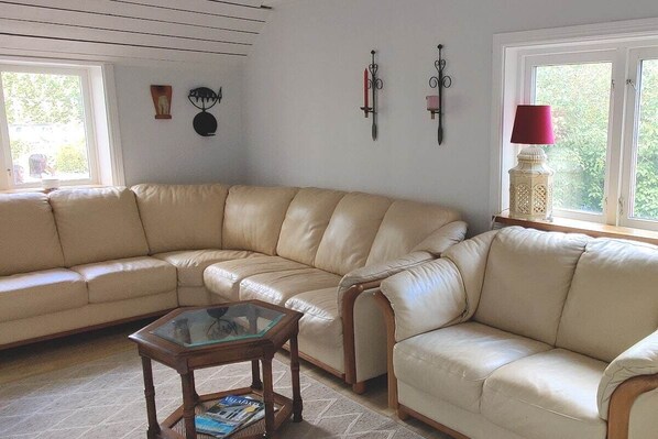 A living room with a beige leather sectional sofa, a glass-top coffee table, and decorative wall sconces.