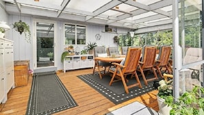 Un invernadero con una mesa y sillas de madera, un armario blanco y plantas colgantes.