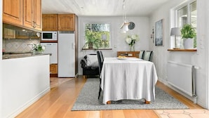 Una cocina moderna con armarios de madera, encimera blanca y comedor con una mesa para dos.