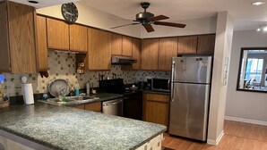 Une cuisine dotée de meubles en bois, d’un plan de travail en granit, d’appareils électroménagers en acier inoxydable et d’un ventilateur de plafond.
