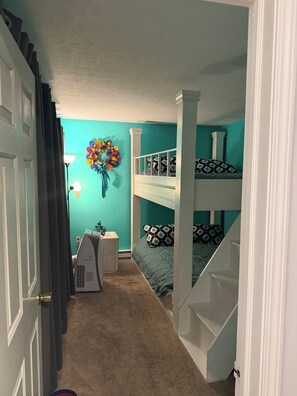 Une chambre avec des lits superposés, un bureau, une lampe et un élément décoratif mural.