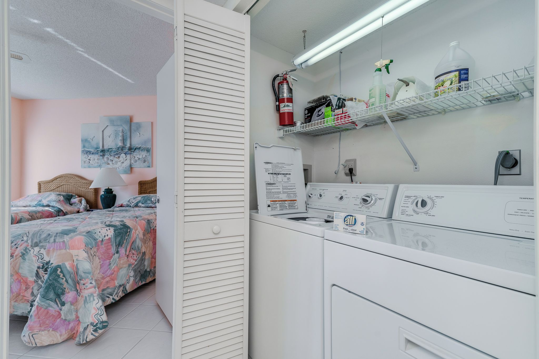 A bedroom with a bed, a nightstand, and a wall-mounted shelf with cleaning supplies.