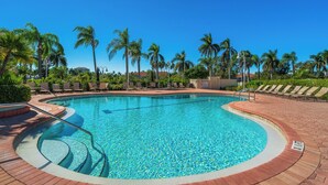 A swimming pool with a curved edge, surrounded by palm trees and lounge chairs. - Vista Verde North 2-110 by Distinctive Beach Rentals (St. Petersburg)