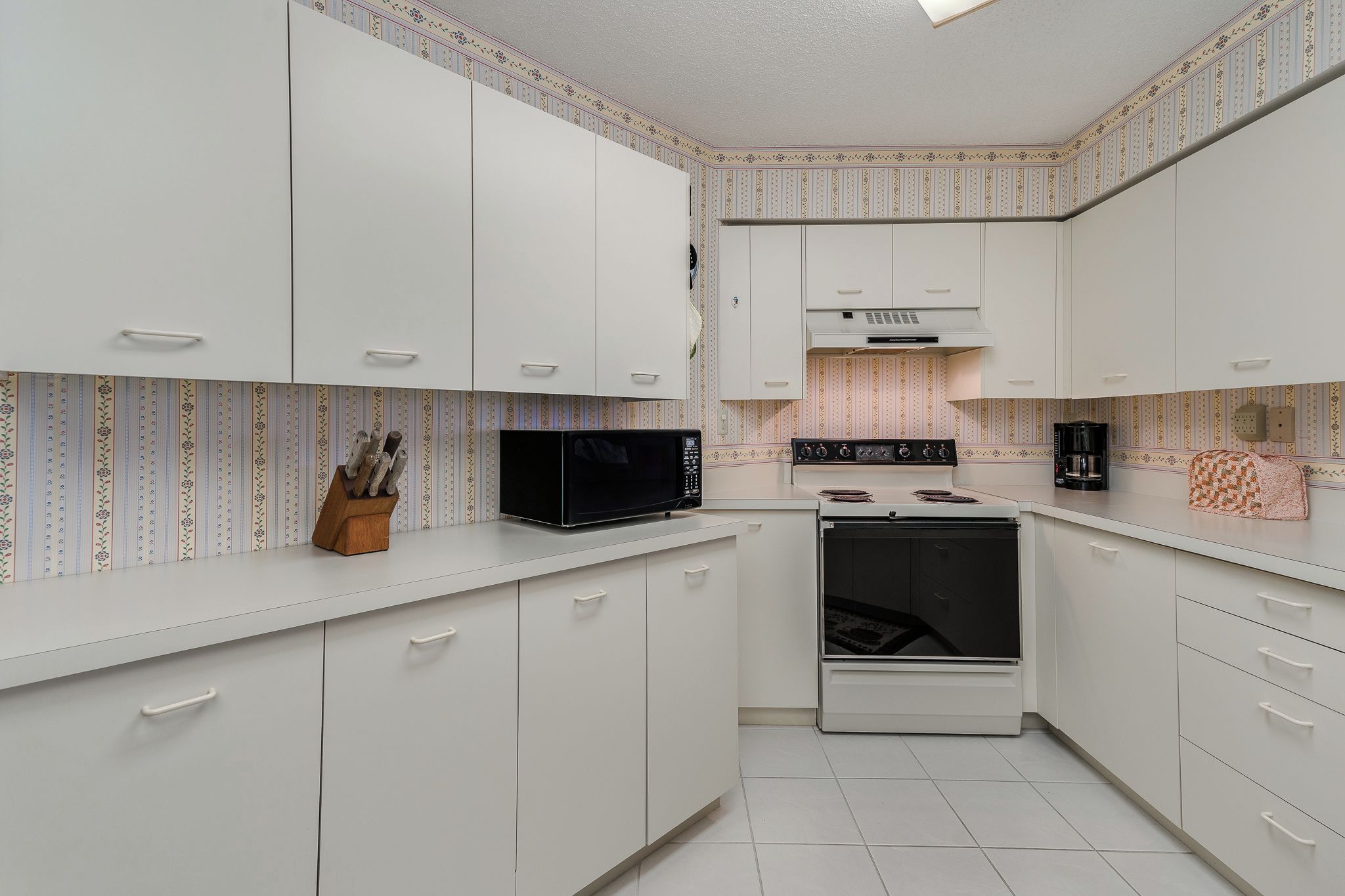 Een moderne keuken met witte kastjes, een magnetron, een fornuis en een koffiezetapparaat.