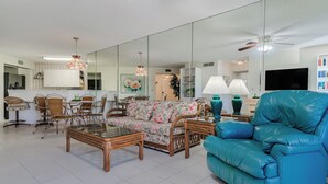 A living room with a sofa, chairs, a coffee table, a TV, and a bookshelf. - Vista Verde North 2-110 by Distinctive Beach Rentals (St. Petersburg)