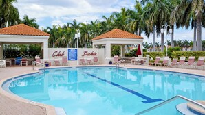 A swimming pool with lounge chairs and umbrellas, surrounded by palm trees and a building with 'Club Baka's' signage. - Bahia Vista 17-881 by Distinctive Beach Rentals (St. Petersburg)