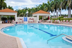 A swimming pool with lounge chairs and umbrellas, surrounded by palm trees and a building with 'Club Baka's' signage. - Bahia Vista 17-881 by Distinctive Beach Rentals (St. Petersburg)