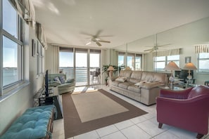 Ein geräumiges Wohnzimmer mit großem Fenster, Deckenventilator, einer Couch, einem roten Sessel und einem Fernseher.