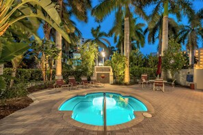 A swimming pool surrounded by palm trees and lounge chairs, with a brick pathway leading to a building. - Bahia Vista 17-881 by Distinctive Beach Rentals (St. Petersburg)
