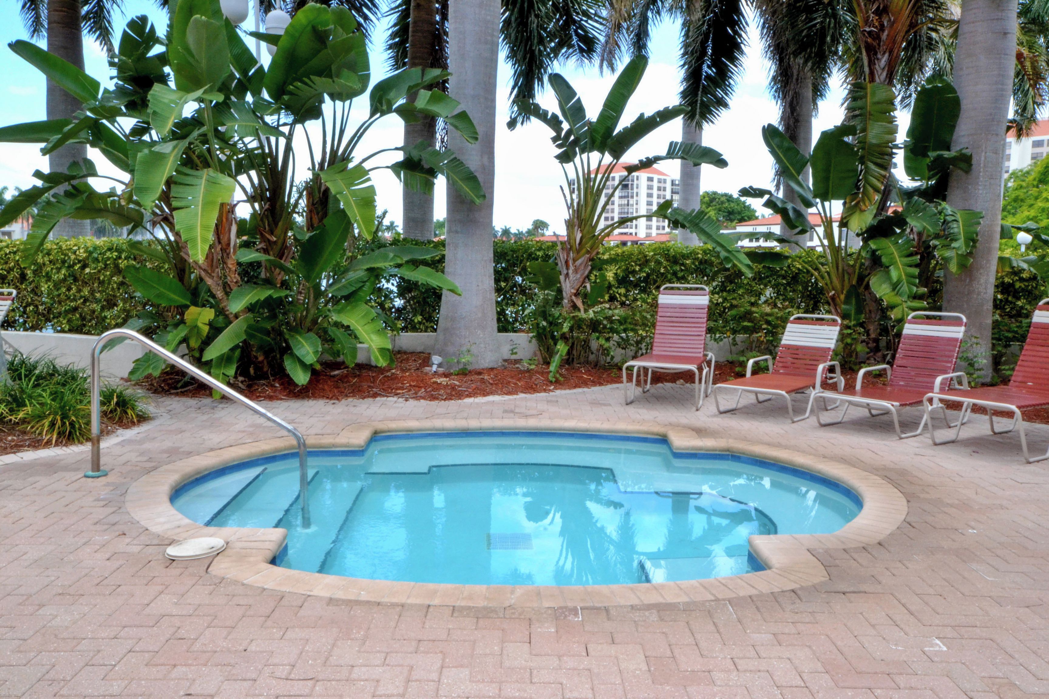 A swimming pool with a brick border, surrounded by palm trees and red lounge chairs.