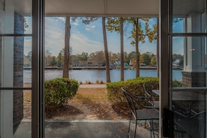 A view from a room with a glass door, overlooking a lake with houses and trees in the background. - Riverwalk 104 (Myrtle Beach)
