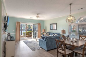 A living room with a sofa, dining table, chairs, and a chandelier. - Riverwalk 104 (Myrtle Beach)