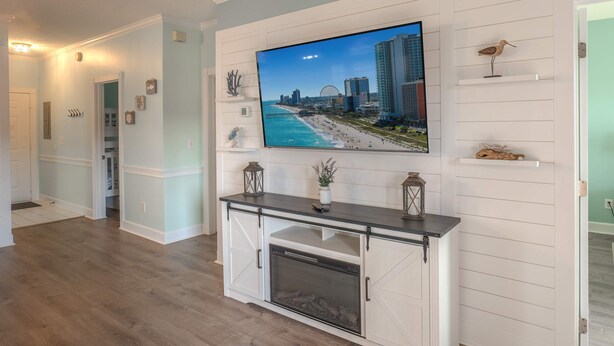 Una sala de estar con un televisor de pantalla plana montado en la pared, una chimenea y un pasillo que conduce a otras habitaciones.