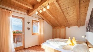 Ein Schlafzimmer mit Holzboden, einem Bett mit weißer Bettwäsche, einem Fenster mit Vorhängen und einem Balkon mit Blumen.