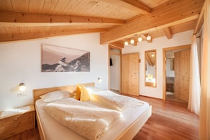 Une chambre avec un plafond en bois, un lit avec une literie blanche, un tableau au mur et un plancher en bois.