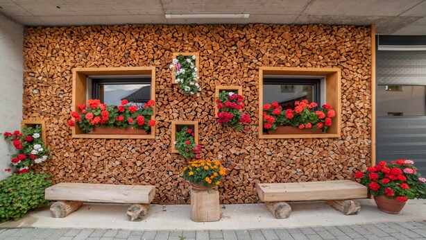 Eine Gebäudefassade mit Holzbalkenwand, Blumenkästen und Bänken.