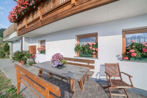 En hvid bygning med træbalkoner, et træbord med bænke og plantekasser med blomster.