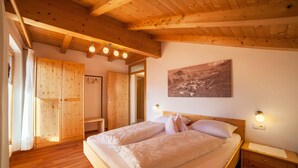 A bedroom with a wooden ceiling, a bed with two pillows, a nightstand, and a wooden wardrobe.