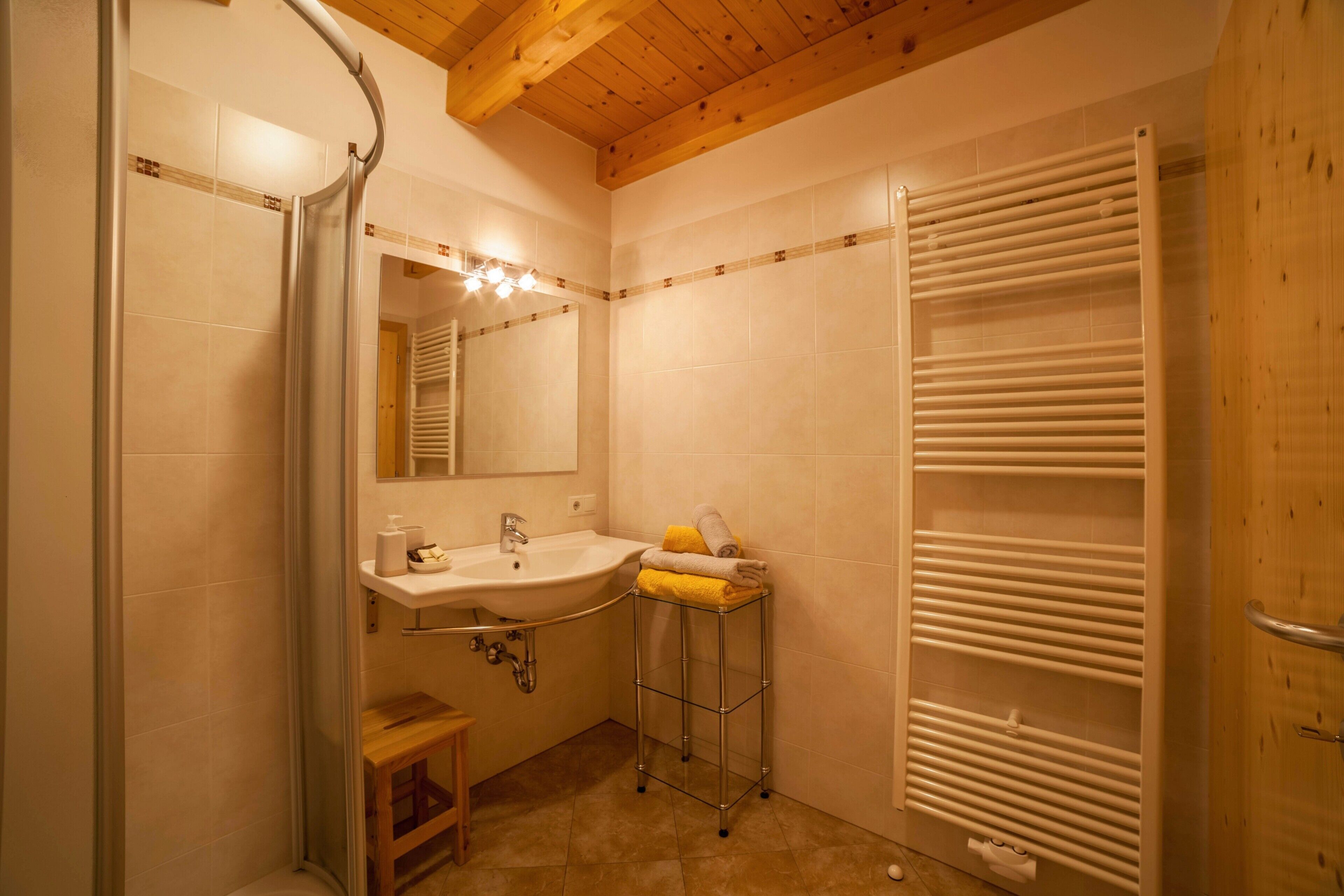 Ein Badezimmer mit Dusche, Waschbecken, Spiegel, Handtuchhalter und Holzboden.
