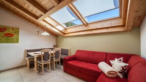 A room with a red sofa, a dining table with chairs, and a skylight.