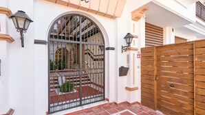 Una entrada protegida con un portón de hierro forjado, cercada por un seto de madera y un patio con baldosas.