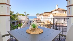 Un balcón con una mesa, una planta en maceta y vistas al mar y edificios.