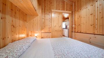 A wooden cabin room with a bed, a small kitchenette, and a wooden ceiling.