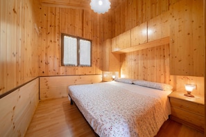 A wooden-paneled room with a bed, bedside table, and a window.
