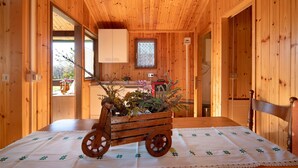 Un interior de madera con una cama, un carro de madera con plantas, una ventana y una zona de cocina.