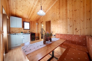L’intérieur d’un chalet en bois comprend une table à manger, des bancs, un coin cuisine et un luminaire suspendu.