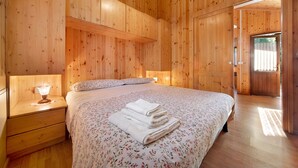 Una habitación con paneles de madera, una cama, una mesita de noche y una puerta que da al exterior.