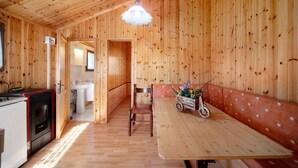 Un interior de madera con una mesa de comedor, sillas, una banca, una zona de cocina y un pasillo que conduce a un baño.